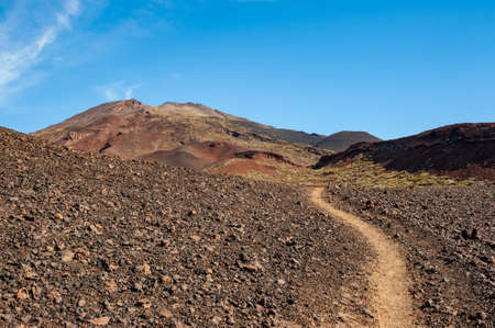 Path in desert and silhouette of volcano del Teide against blue sky and female hiker with backpack. Pico del Teide mountain in El Teide National park. Tenerife, Canary Islands, Spainの写真素材