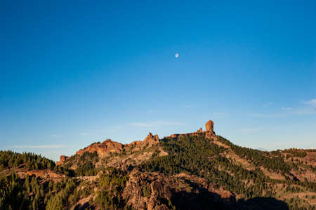 Roque Nublo, symbolic natural monument of Gran Canaria, Canary Islands. Summer sunny day with blue skies and moon and cloud sky. Emblematic volcanic rock formations in the mountains of Gran Canaria Spain.の写真素材