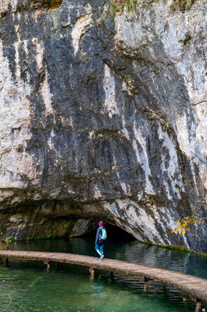 Young woman tourist walking in Plitvice Lakes National Park during colorful autumn, Croatia, Europe. Female enjoying fall colors. Waterfalls and water. Landscape photography. View of Plitvice Lakes.の写真素材