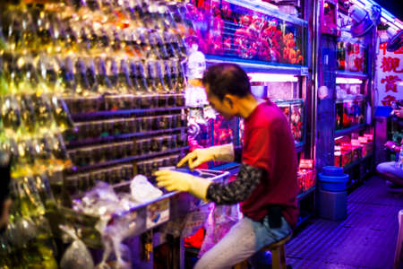 Hong Kong, China - 7 July, 2013: Shopkeeper surrounded by many bags with exotic fish on Tung Choi Street in Mongkok. Focus on tanks behind employeeのeditorial素材
