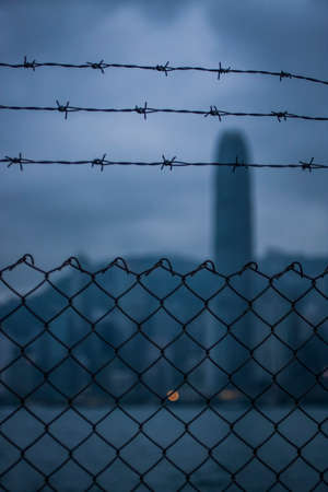 Chain link fence and barbed wire with silhouette of Hong Kong's skylineの写真素材