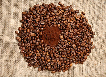 Ground Coffee Surrounded by Roasted Coffee Beans on Burlapの写真素材