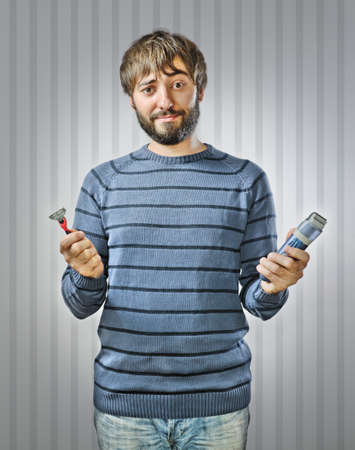 Unshaved Young Man Choosing between Razor and Hair Clipperの写真素材