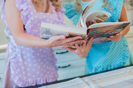 two girls reading a recipe book in apronsの写真素材