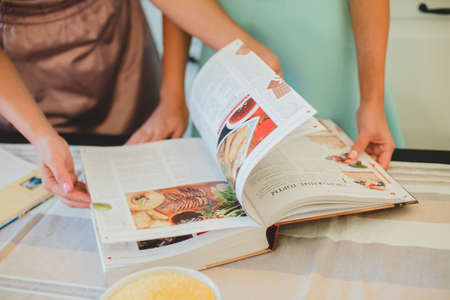 two girls reading a recipe book in apronsの写真素材