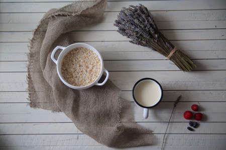 oatmeal porridge, bottle of milk and berries on wooden background with kitchen towel, top viewの写真素材