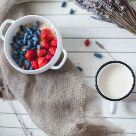 oatmeal porridge, bottle of milk and berries on wooden background with kitchen towel, top viewの写真素材