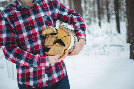 a man in a checkered shirt carries a pile of firewood in the winter forestの写真素材