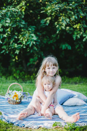 two sisters hugging on a picnic sitting on a blanketの写真素材