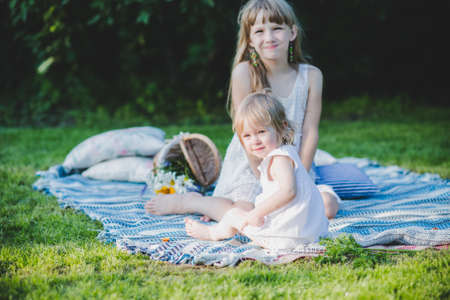 two sisters hugging on a picnic sitting on a blanketの写真素材