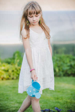 beautiful little girl standing with a watering can in the gardenの写真素材