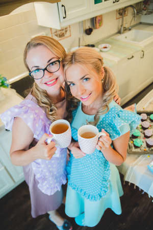 two women in kitchen drinking a cup of teaの写真素材