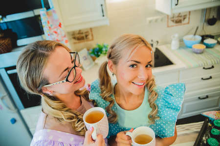 two women in kitchen drinking a cup of teaの写真素材