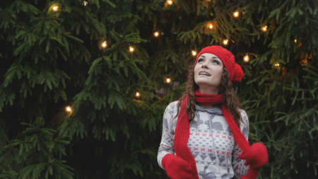 Cheerful woman in Santa hat with red scarf and mittens is happy and jumping against the background...
