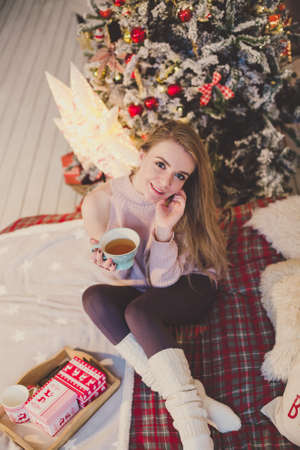 young woman in christmas interior. Sit with a plaid and a cup of tea.の写真素材