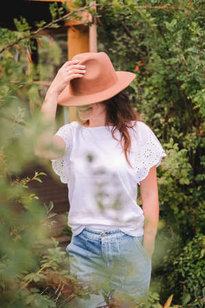 Attractive brunette in a hat and white shirt is enjoying nature in the mountains. Beautiful young woman in a shirt and jeans walks along the beautiful landscapeの写真素材