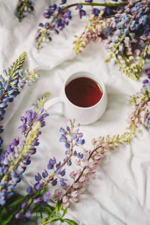spring composition with flowers and a cup of tea on a white sheet. flowers and a cup of coffee among the flowers. Flat lay, top viewの写真素材