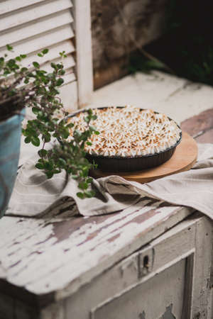 beautiful pie with white meringue cream on a wooden white plate among summer greens. Viewpoint from above.の写真素材