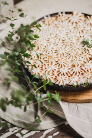 beautiful pie with white meringue cream on a wooden white plate among summer greens. Viewpoint from above.の写真素材