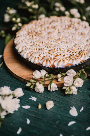 beautiful pie with white meringue cream on a wooden background among white flowers. Viewpoint from above.の写真素材