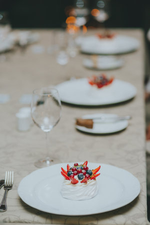 Photo of female hands cutting a fruit cake with strawberries, mint and black currants on a white...