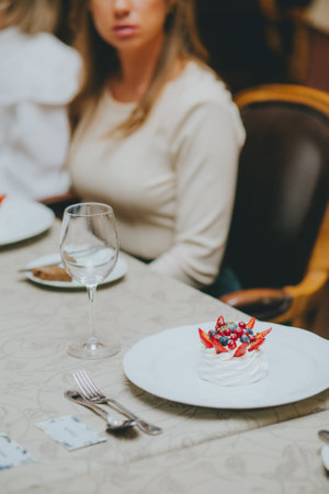 Photo of female hands cutting a fruit cake with strawberries, mint and black currants on a white plate on a table in a restaurant. dessert pavlova. table etiquetteの写真素材