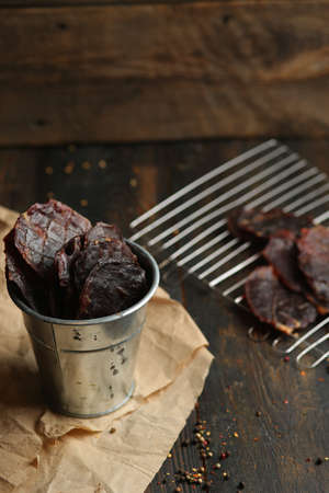 Homemade beef jerky seasoned with garlic, onion, pepper and salt. Jerky in a bucket on a wooden backgroundの写真素材