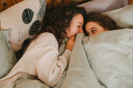 Happy young woman with cute teenage daughter posing in bedの写真素材