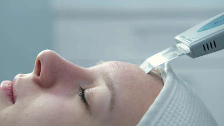 Doctor with ultrasonic scraber. Procedure of ultrasonic cleaning of face. Patient in beauty clinic....
