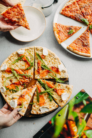 Traditional Italian pizza, vegetables, ingredients on a light background.Top view. a piece of pizza in the hand.Festive table. company of friendsの写真素材