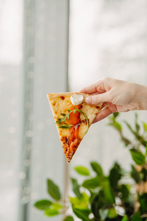 A piece of pizza in his hand, against the backdrop of the restaurant, Side view of the pizza. The concept of Italian cuisine, street food, fast food, fast food. Bannerの写真素材