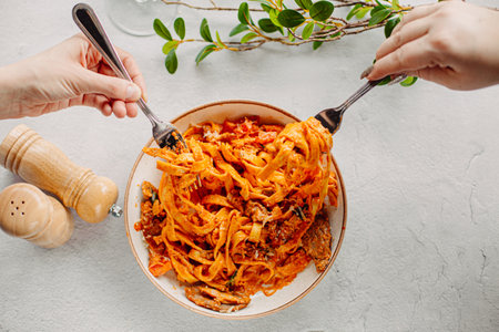 Italian pasta, tomato sauce. Two female hands in the frame, girls eat pasta, hold forks in their hands, top view, Italian cuisine.の写真素材