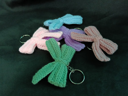 many handmade crochet keychains featuring bow designs in pastel colors lie on a black fabric. photo...
