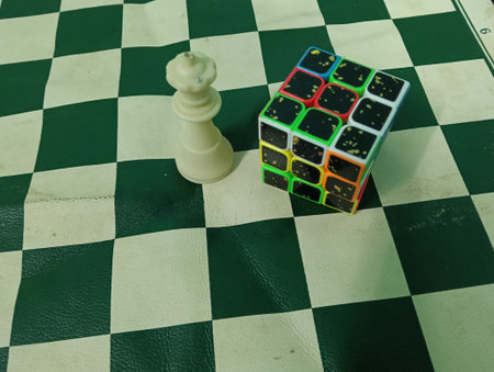Queen Chess piece and rubic cube on a green and black checkered chessboard. symbolic of mind game...