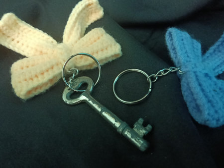 Three handmade crochet keychains and a key featuring bow designs in pastel colors lie on a black...