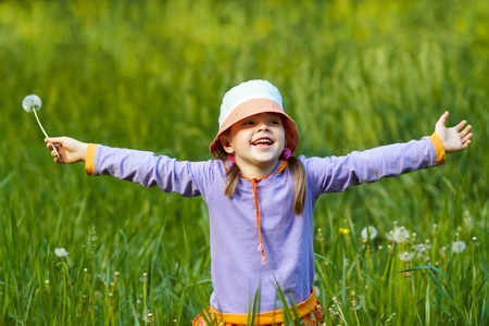 happy girl with dandelion arms outstretched against a background of green grassの写真素材