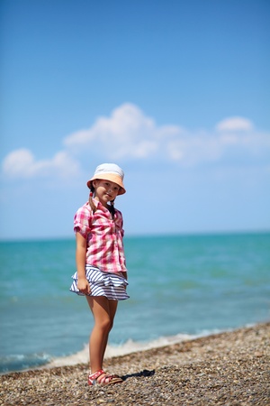 girl in a hat standing on the pebbly sea beachの写真素材