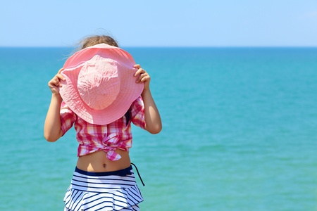 Girl hiding behind a pink hat on a background of the seaの写真素材