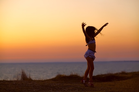 silhouette of a dancing girl with hands raised in the sunset on the sea backgroundの写真素材
