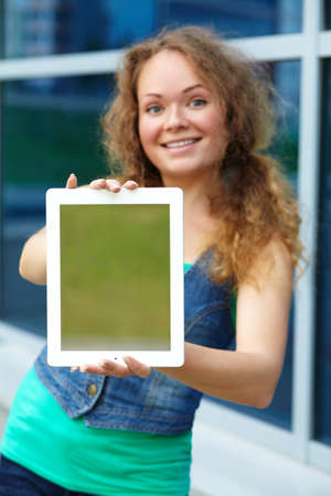 Pretty smiling young girl holding a tablet computer on the background office building, focus on the tabletの写真素材