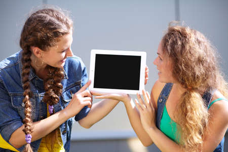 Two girls with a look at the tablet computer on the gray background