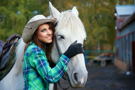 cute smiling cowgirl in a hat with a white horseの写真素材