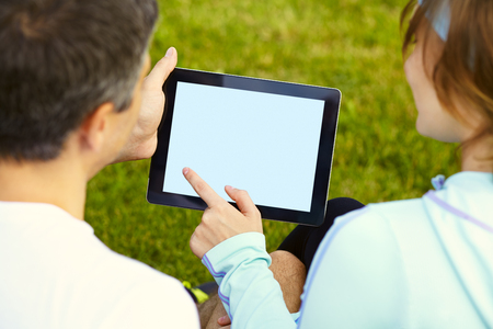 sports couple sitting on the grass using a digital tablet after trainingの写真素材