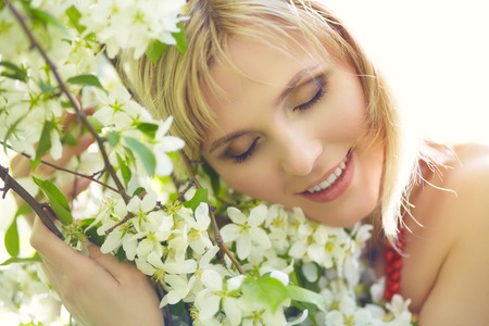 outdoor closeup portrait of a beautiful blonde woman among blossom apple treesの写真素材