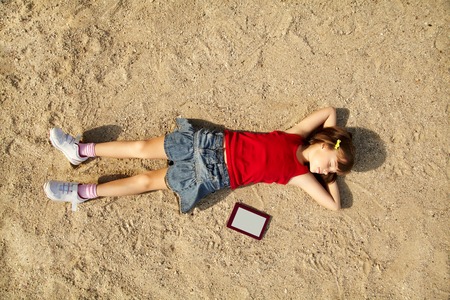 little girl lying on the sand with a tablet computer の写真素材