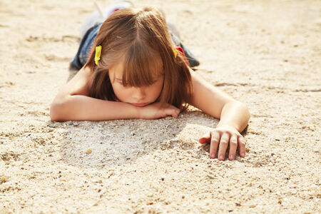 thoughtful little girl lying on the sand  の写真素材