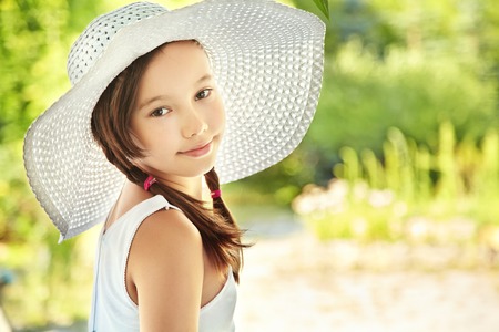 portrait of a cute teenage girl in wide-brimmed hat on a background of green in summer parkの写真素材