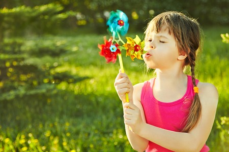 cheerful little girl playing with pinwheel in the park on a green backgroundの写真素材