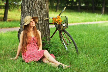 young woman in a hat with a bike sitting in the park near the tree . Active people. Outdoorsの写真素材
