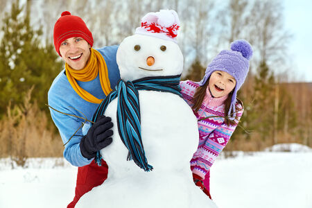 funny dad and daughter with a snowman in winterの写真素材